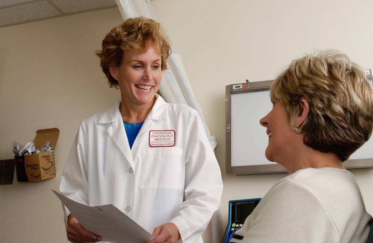 A clinician in a white coat reviewing a chart and talking with a colleague in a clinic room