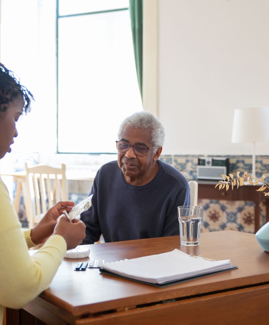 A care worker going through medication with an older man at his kitchen table